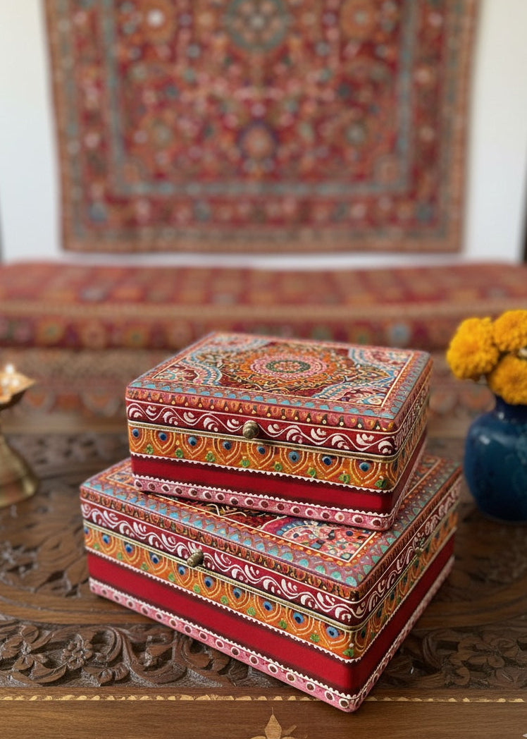 Decorative boxes with intricate patterns on a wooden table, with a colourful tapestry in the background.