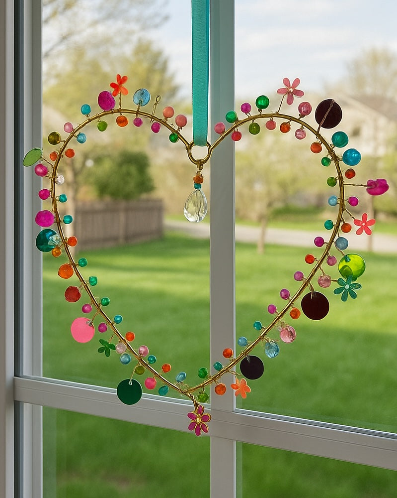 Decorative heart-shaped hanging with colourful beads and flowers sequins on a glass window