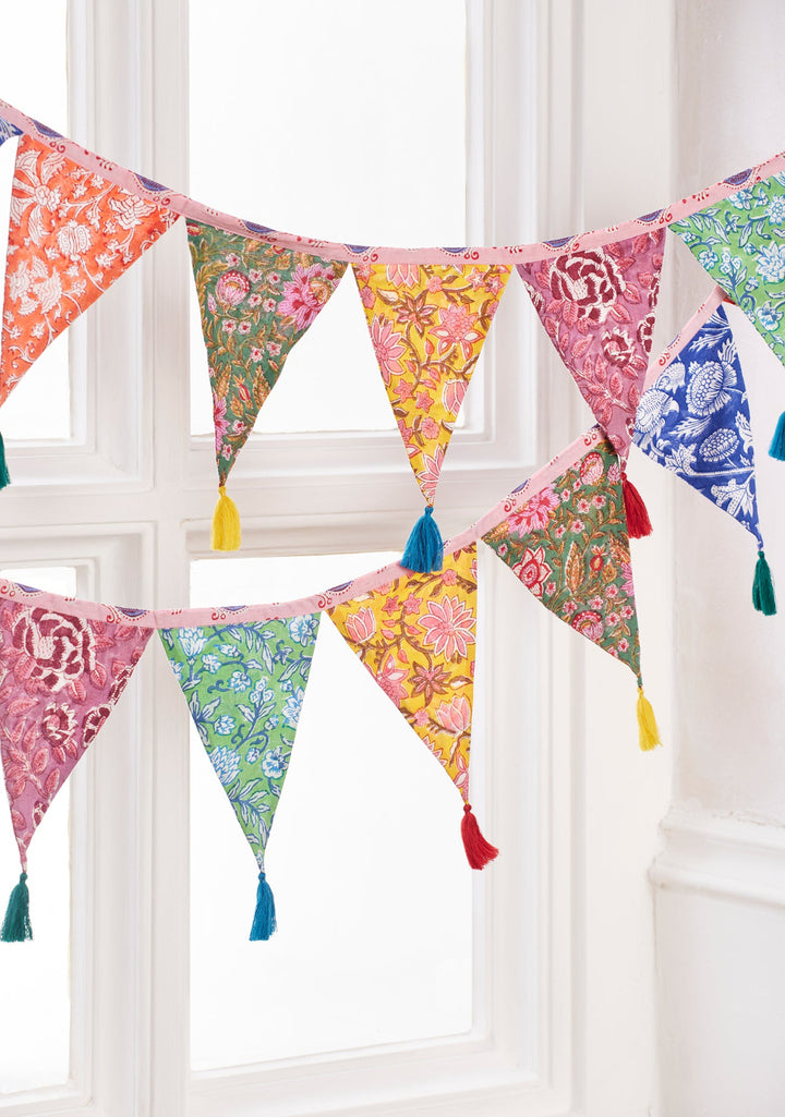 Colourful fabric bunting with tassels hanging against a white window frame.