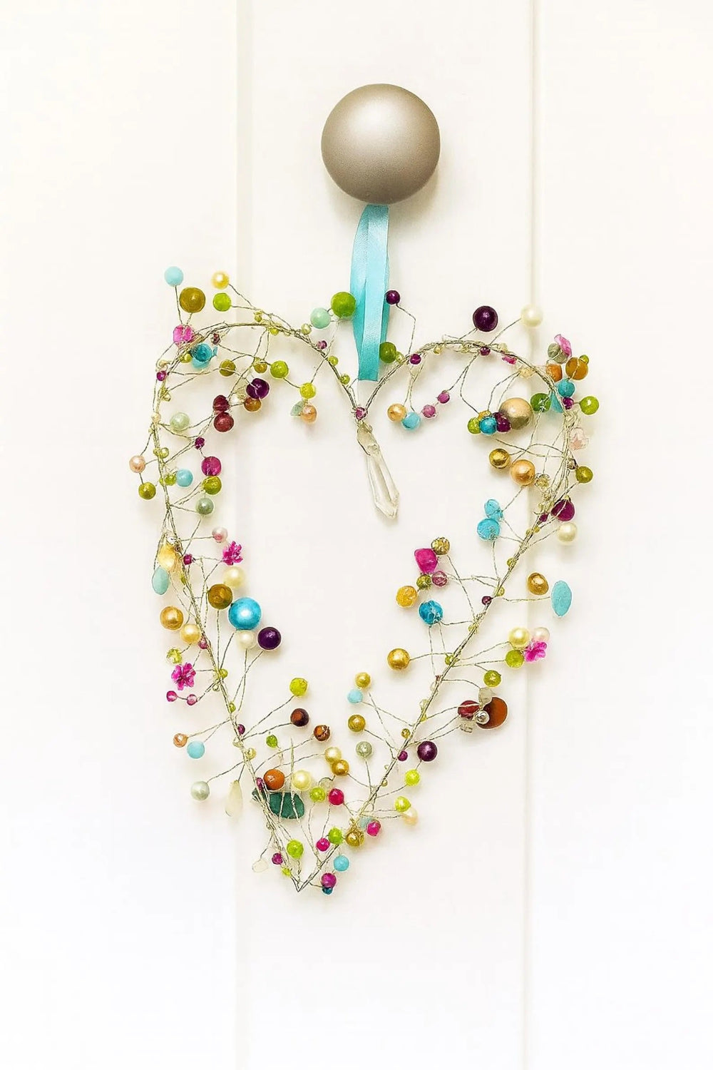 Decorative heart-shaped ornament with colourful beads and a silver handle on a white background