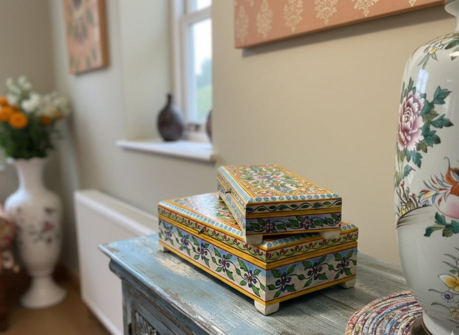 Decorative boxes with floral patterns on a wooden box, with a blurred background of a room.