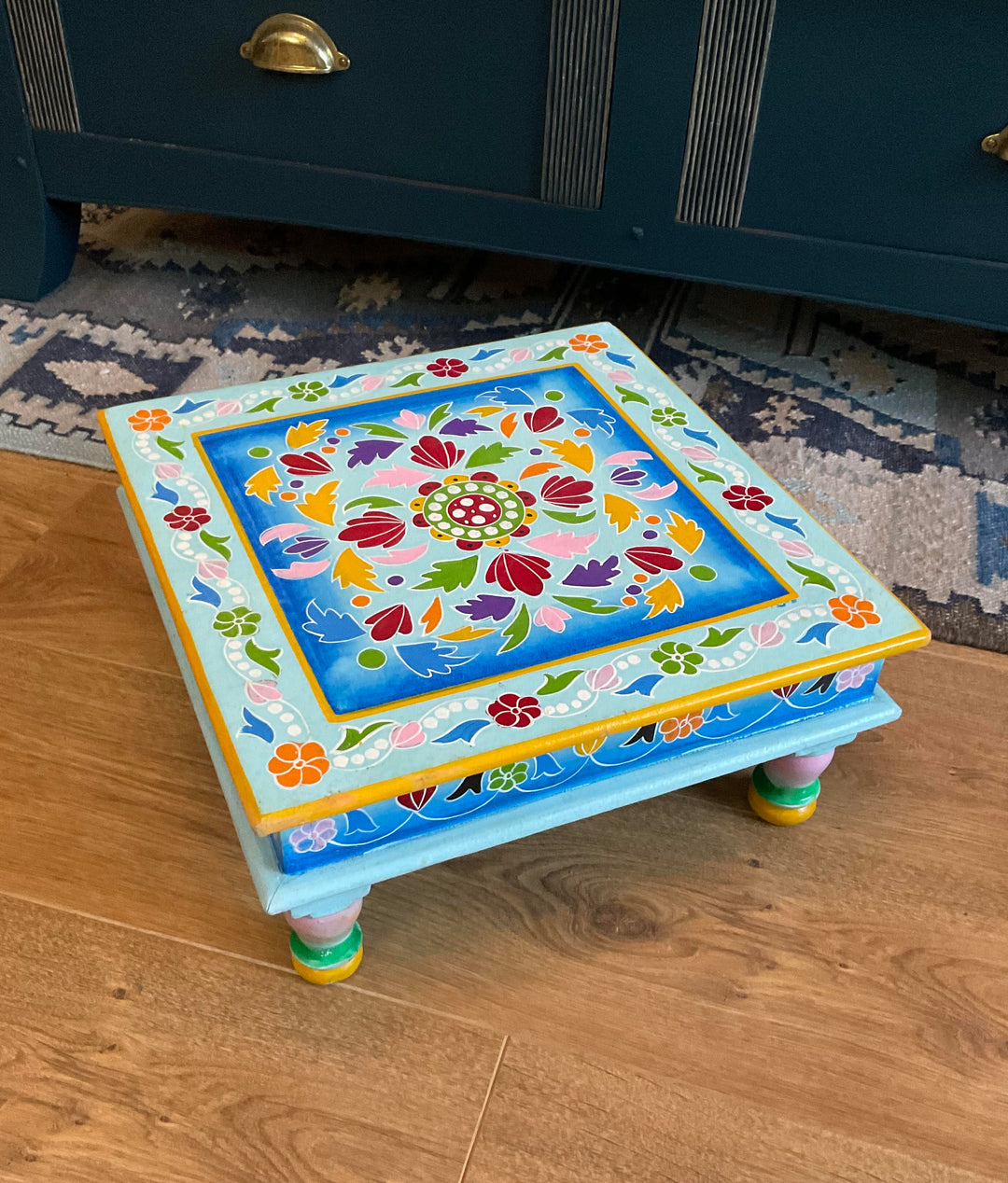 Colourful decorative step stool on a wooden floor with a dark blue cabinet in the background.