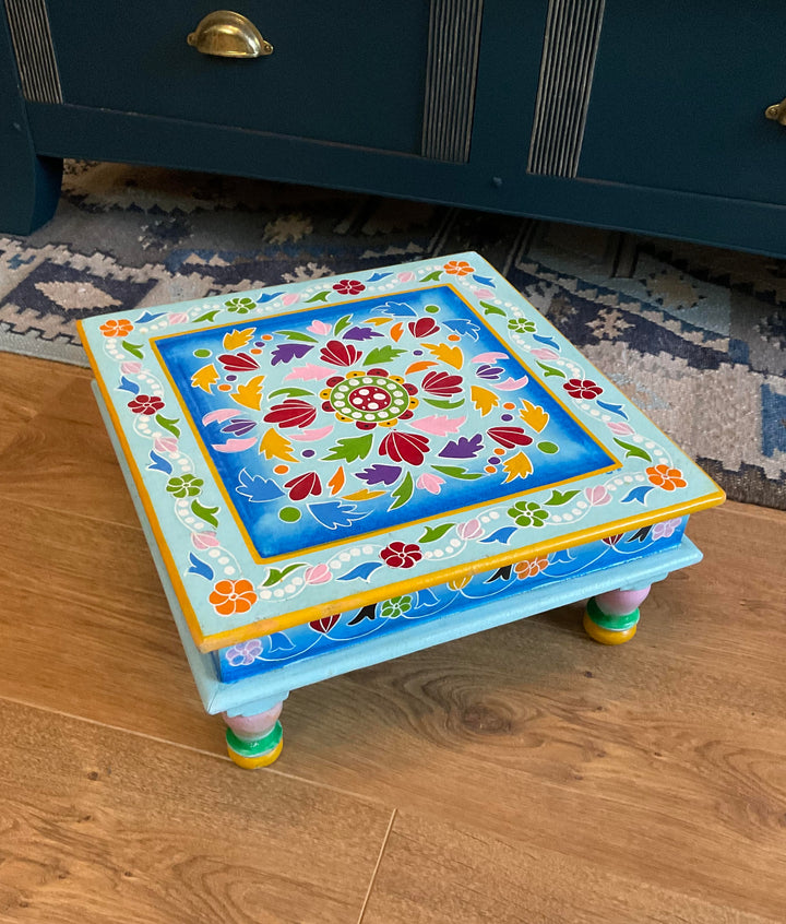 Colourful decorative step stool on a wooden floor with a dark blue cabinet in the background.