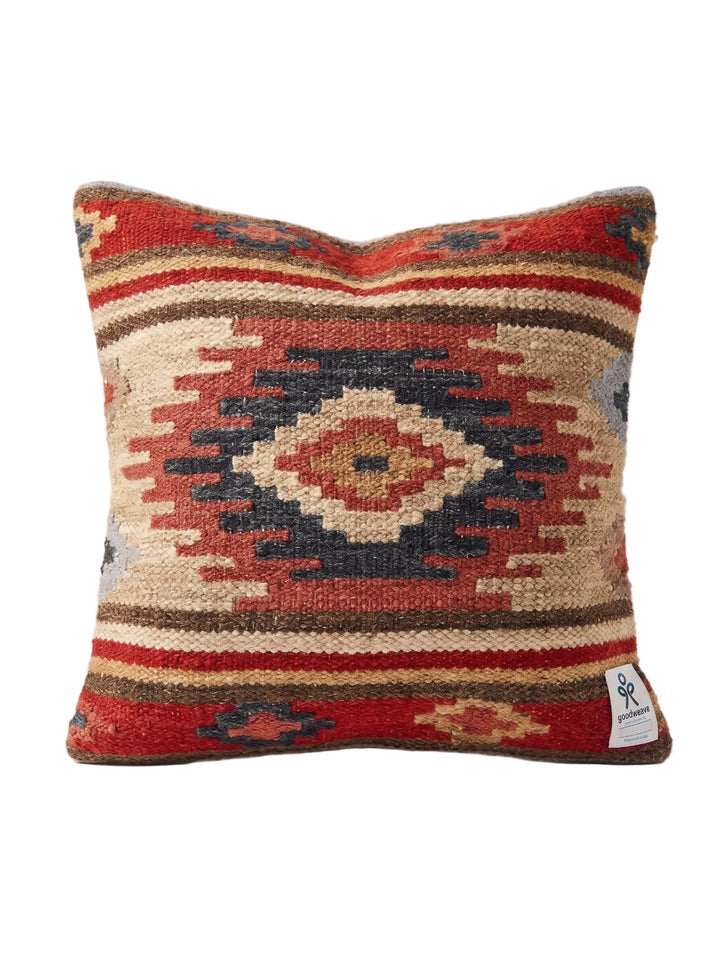 A square woven throw pillow featuring a Southwestern geometric pattern in red, beige, brown, and navy blue, with a small white brand tag on the bottom right corner.
