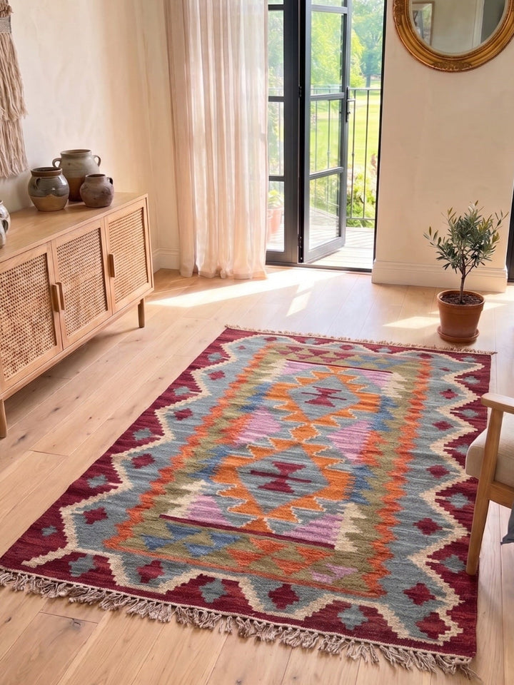 Kilim with a multi colour pattern with a sideboard, plant and chair.