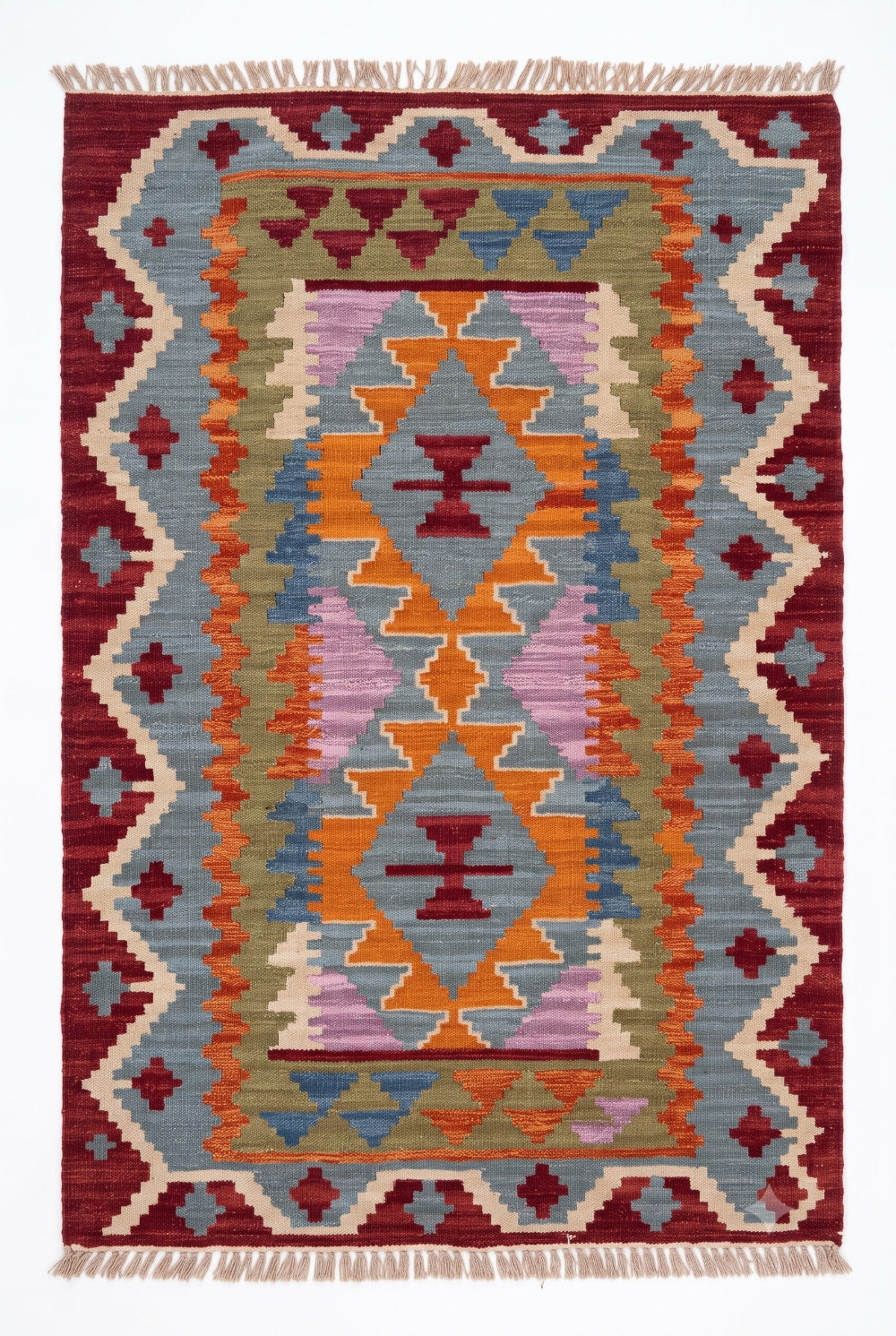 A rectangular woven rug with a Southwestern geometric pattern, featuring a central diamond motif in orange, yellow, and purple, surrounded by blue, green, and red bands, finished with fringe on the top and bottom edges.