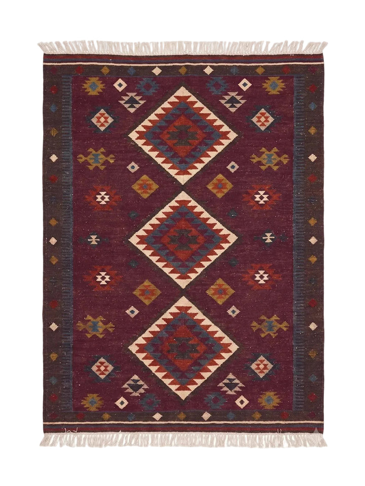 A rectangular woven area rug with a traditional geometric pattern, featuring large central diamond motifs and fringe on the top and bottom edges. The dominant color is a deep burgundy, with accents of cream, rust orange, and blue.