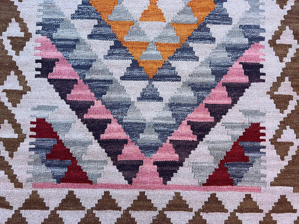 A close-up of a woven geometric textile with repeating triangle patterns in pink, navy, grey, mustard yellow, and dark red on a light base.