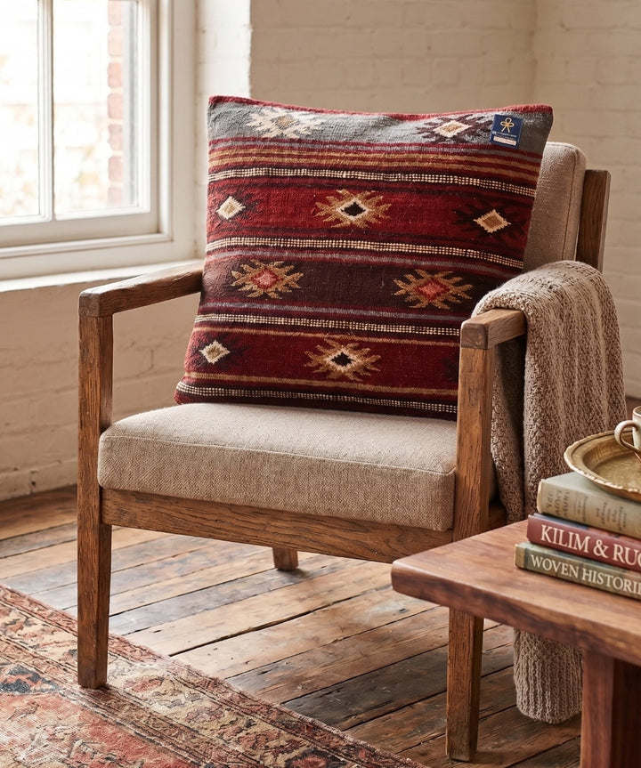 Wooden armchair with a patterned pillow and books on a wooden table in a room with a window.