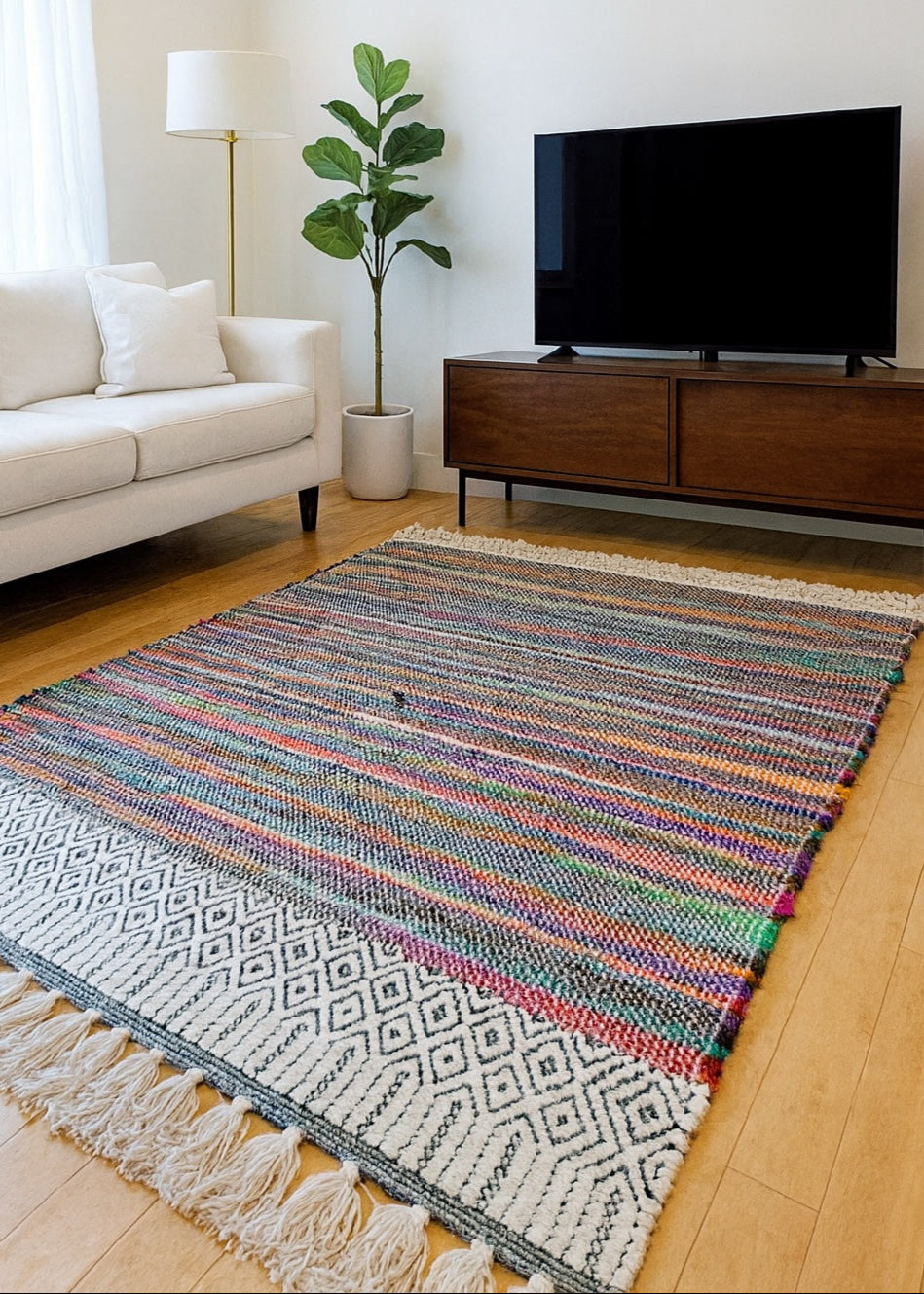 Living room with a colourful rug, white sofa, and TV on a wooden stand.