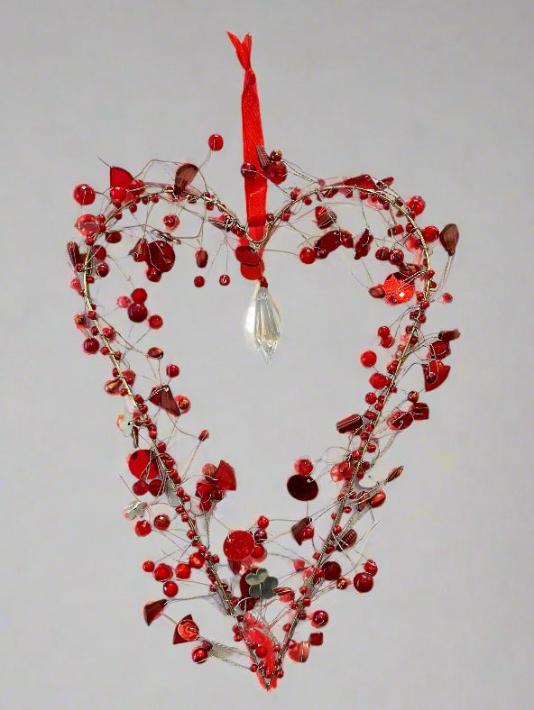 Decorative heart-shaped ornament with red berries and a red ribbon on a grey background