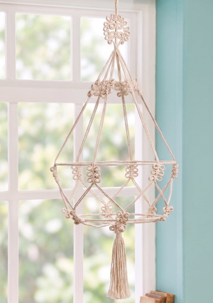 Decorative macrame hanging with tassels against a light blue wall and window.