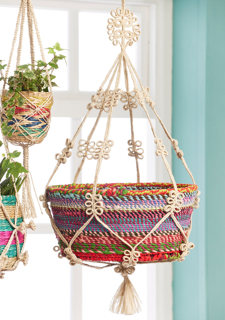 Colourful woven plant hanger with tassels against a light blue wall.