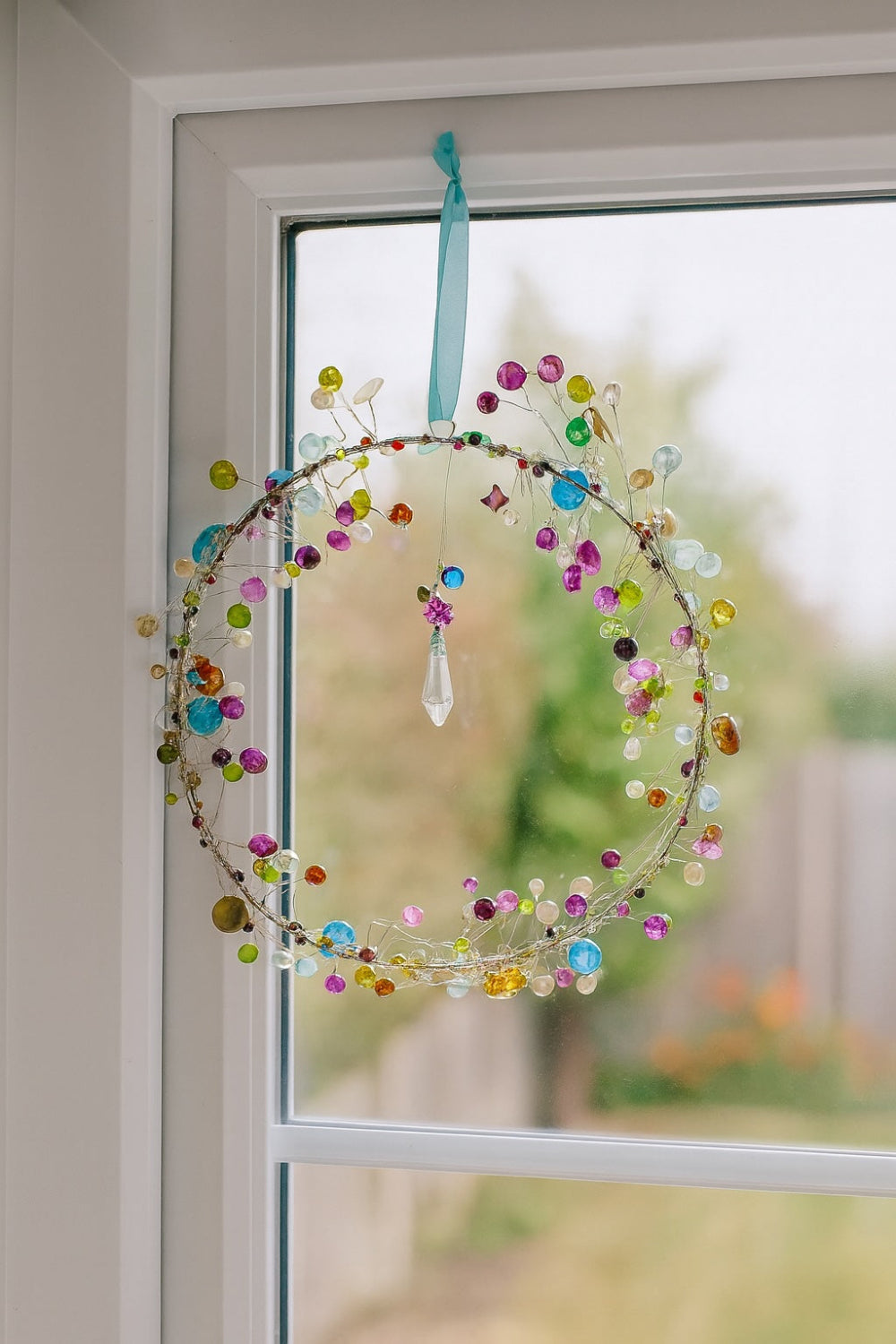 Decorative glass hanging with colourful beads and a crystal in a window