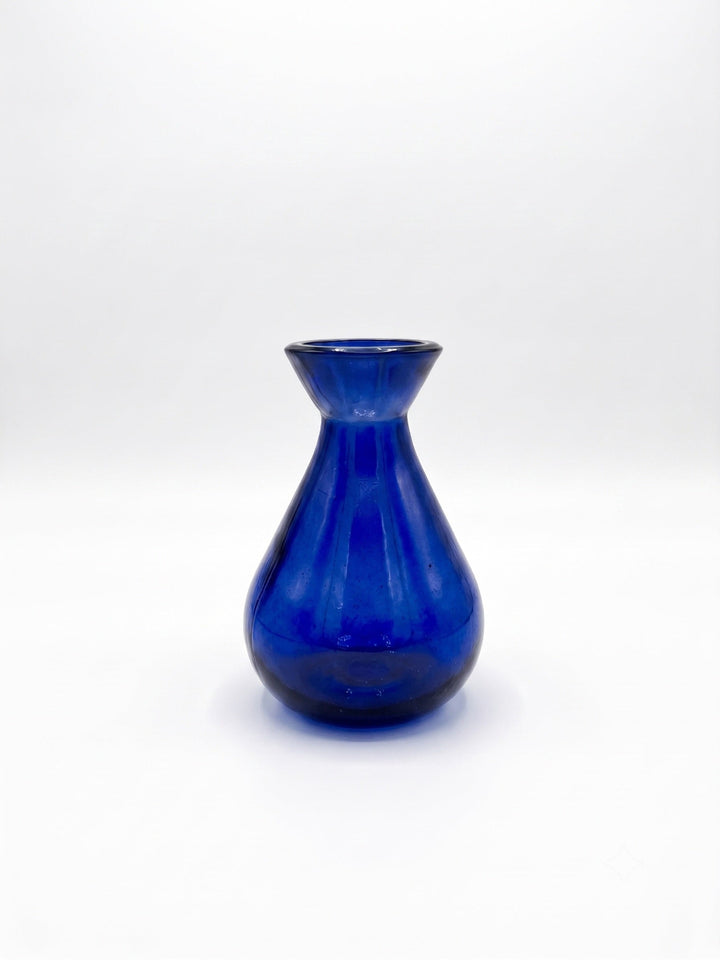 A small cobalt blue glass vase with a flared rim and ribbed body, centered on a plain white studio background.