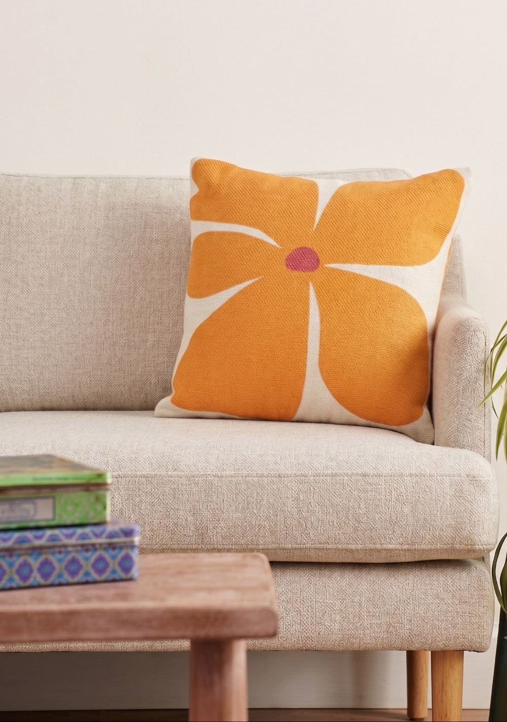 Orange floral pillow on a beige sofa with a wooden coffee table and plant in the background.