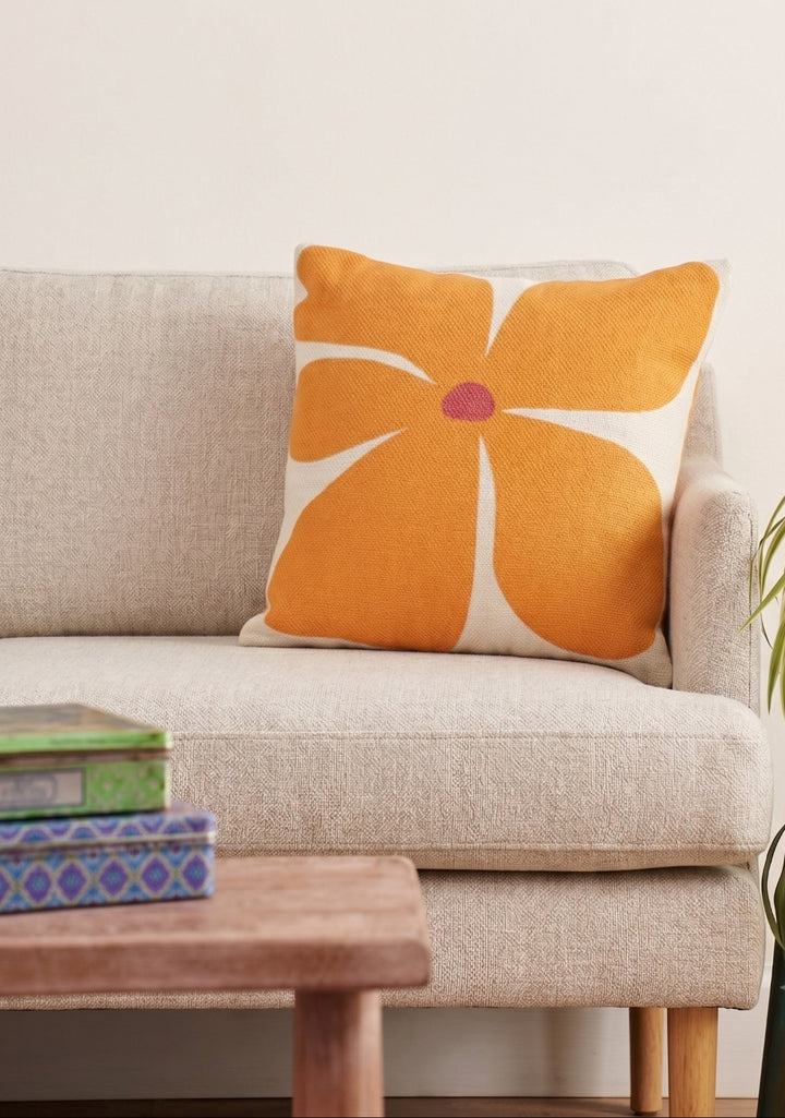 Orange floral pillow on a beige sofa with a wooden coffee table and plant in the background.