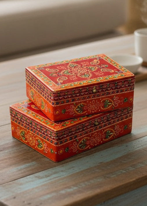 Two decorative orange boxes with intricate patterns on a wooden surface.