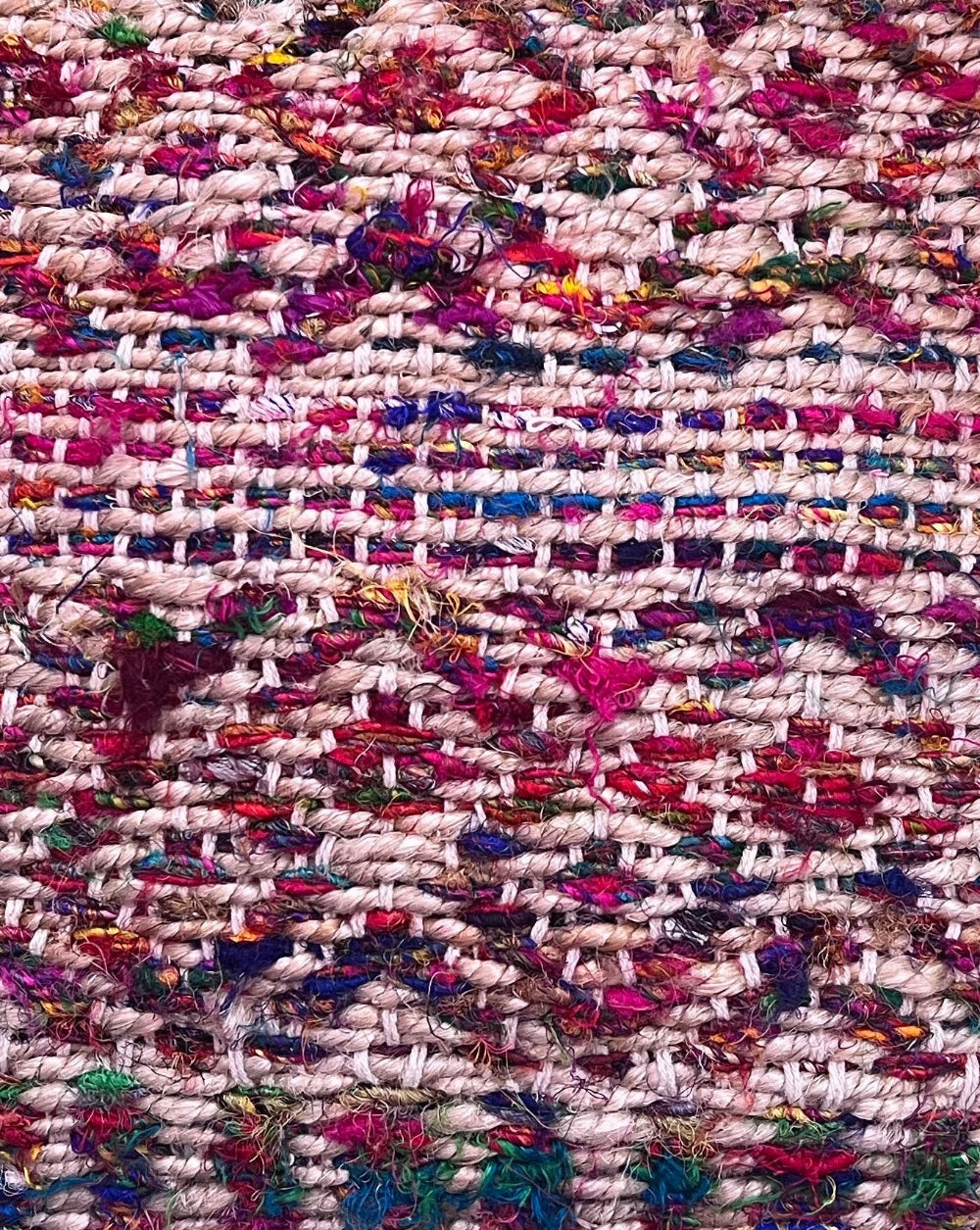A close-up of a woven textile with a chunky, textured pattern in cream, pink, red, blue, green, and purple.