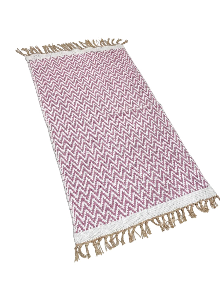 A rectangular woven throw blanket with a pink and white chevron pattern and natural beige fringe on all ends, laid flat on a white background.