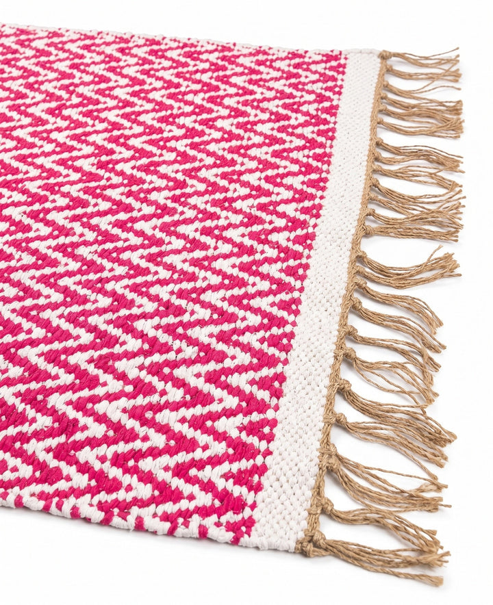 Pink and white zigzag patterned rug with brown fringes on a white background