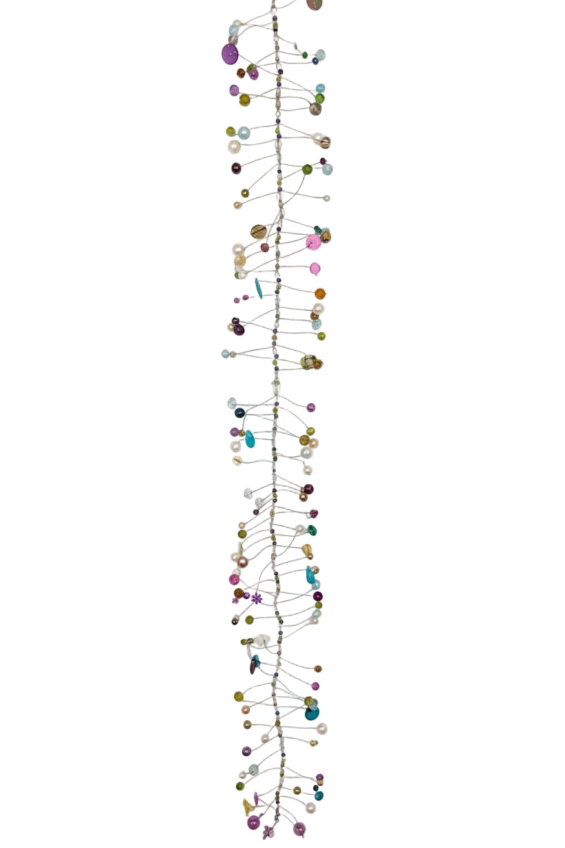 A long, narrow wall hanging decoration made of a vertical metal wire frame decorated with many small colourful beads, pins, and hanging elements, photographed against a plain white wall.