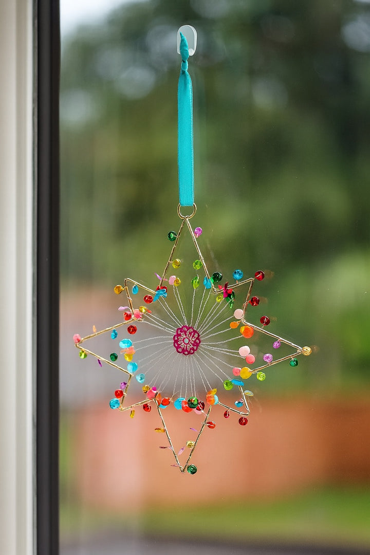 Decorative star-shaped hanging ornament with colourful beads on a blurred natural background