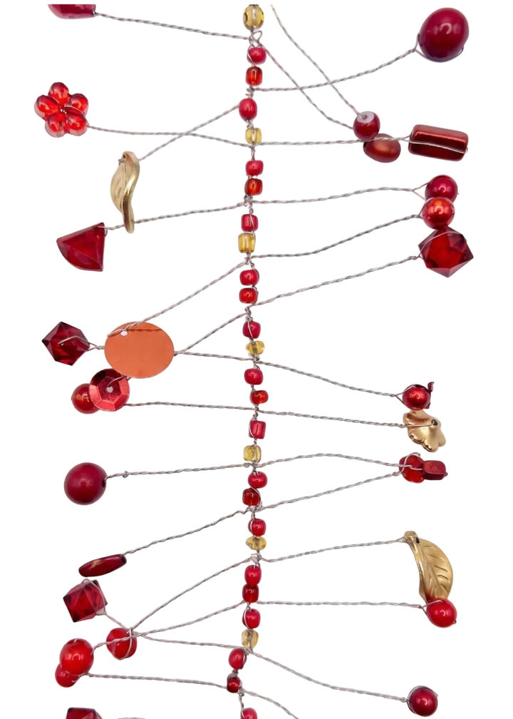A decorative hanging garland made of thin wire with multiple red beads, red glass accents, a few translucent amber/yellow beads, and a few metallic gold leaf-shaped charms, laid flat on a white background.