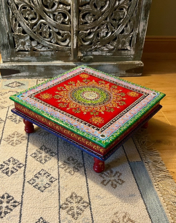 Decorative wooden stool with colorful patterns on a patterned rug.