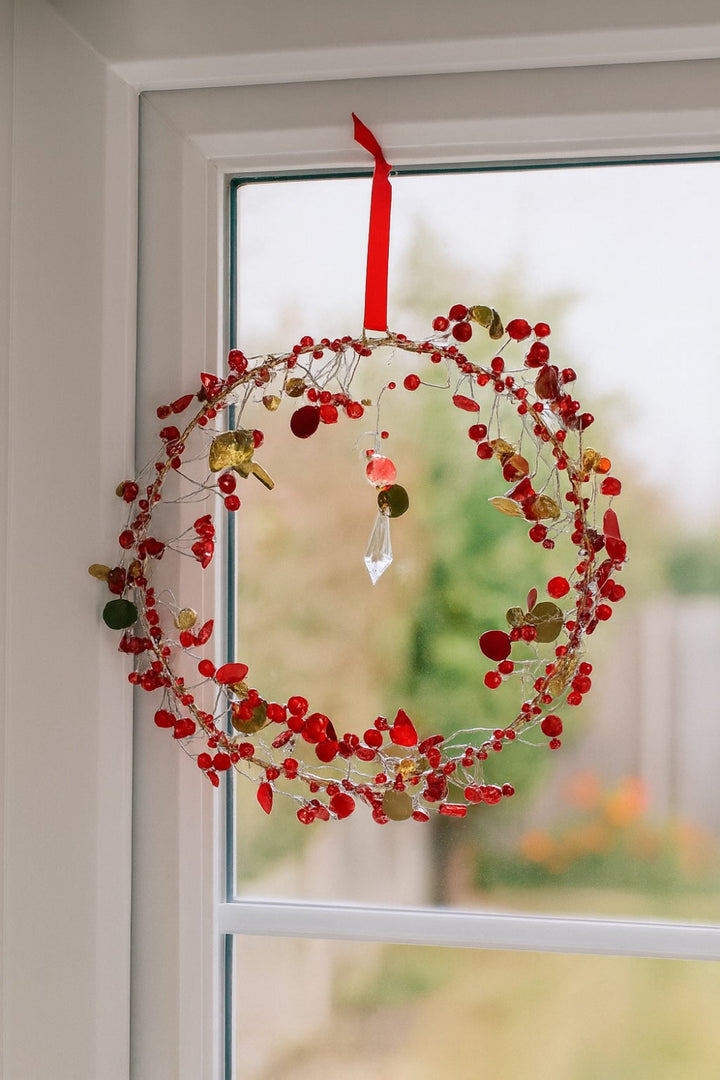 Decorative wreath with red berries beads and a crystal hanging on a window