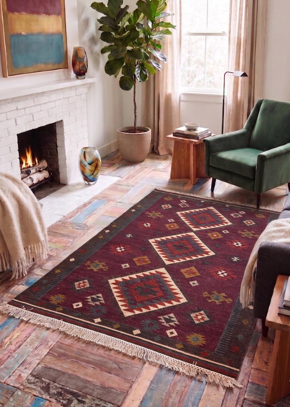 A rectangular area rug with a Southwestern geometric pattern in deep red, beige, and blue, styled on a rustic wood floor in a cosy living room with a fireplace, green armchair, and sofa.