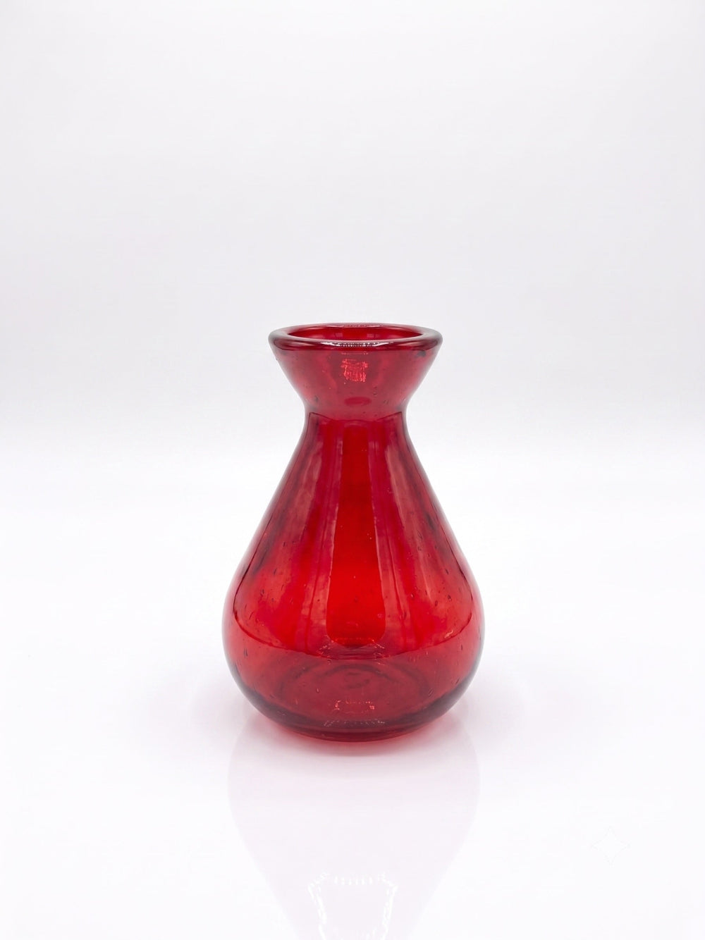 A small red glass vase with a flared rim and bulbous base, photographed on a clean white studio background with a soft reflection below.