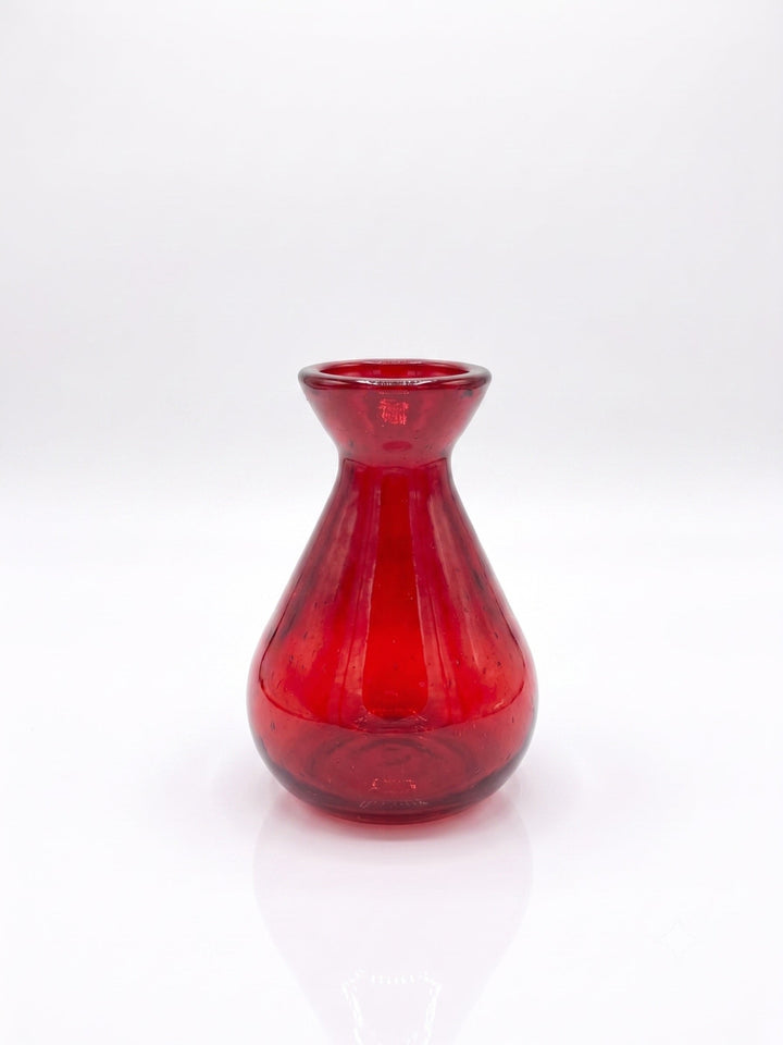 A small red glass vase with a flared rim and bulbous base, photographed on a clean white studio background with a soft reflection below.