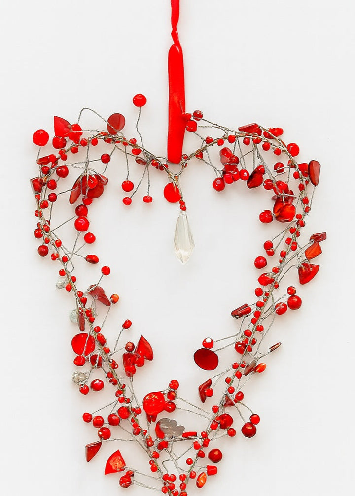 Heart-shaped decoration with red berries and a red string on a white background