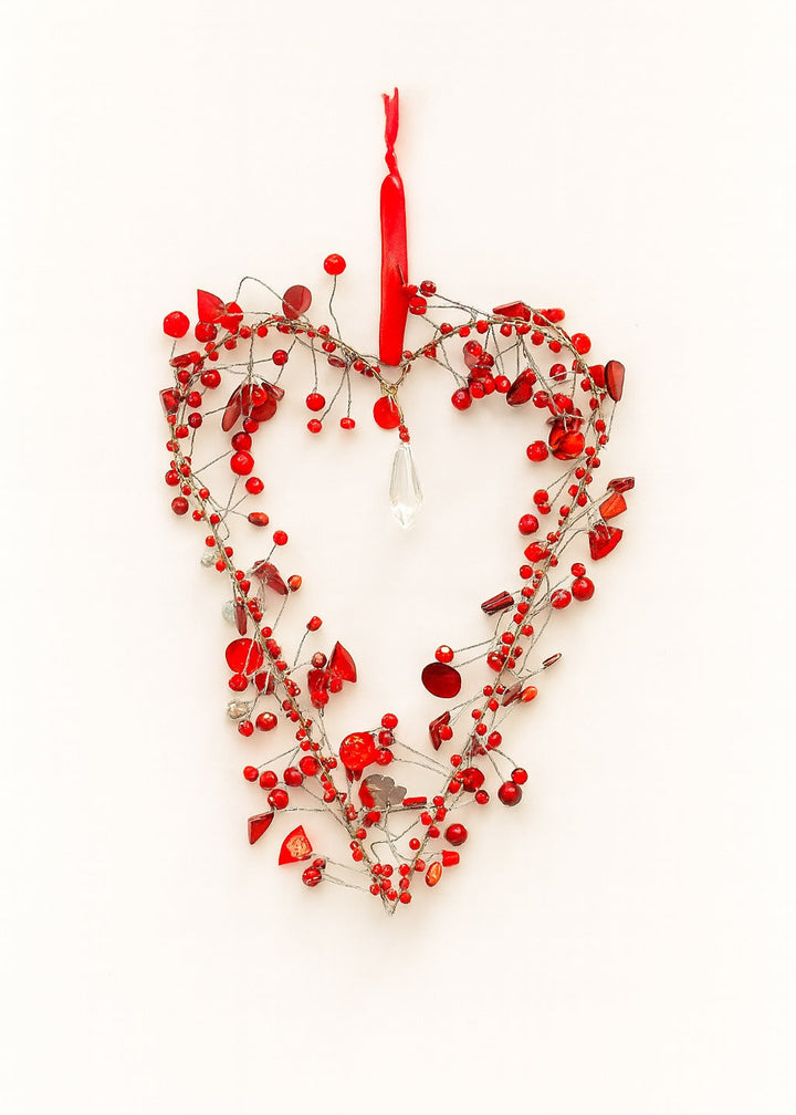 Heart-shaped decorative wreath with red berry beads and a red ribbon on a white background