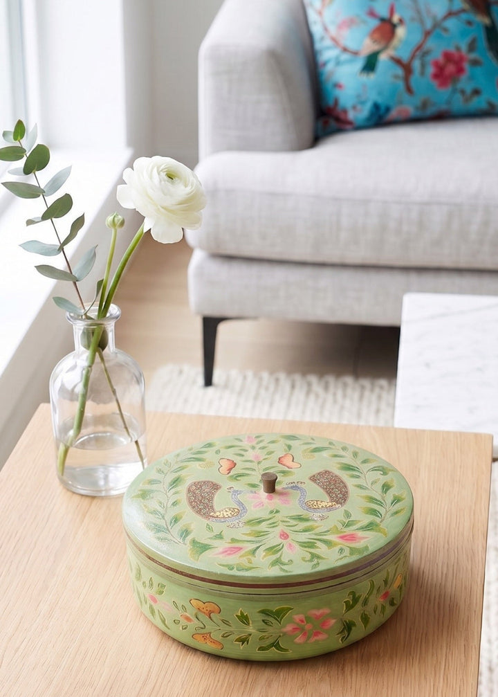 Decorative green box on a wooden table with a couch and floral pillow in the background