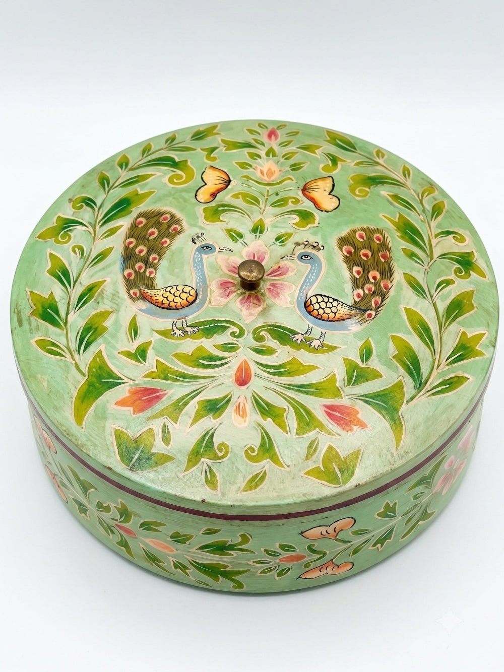 Decorative round box with peacock and floral patterns on a light green background