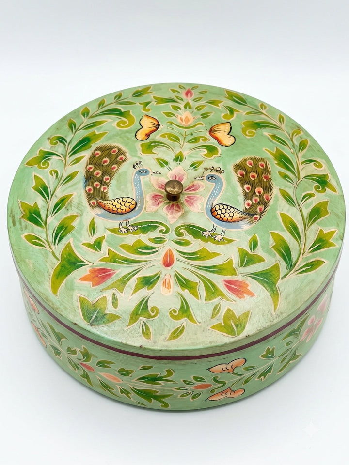Decorative round box with peacock and floral patterns on a light green background