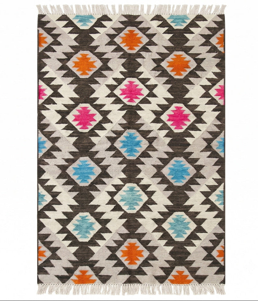 A rectangular woven area rug with a Southwestern geometric pattern, featuring dark brown, cream, black, orange, pink, and light blue diamond motifs with white fringe on the top and bottom.