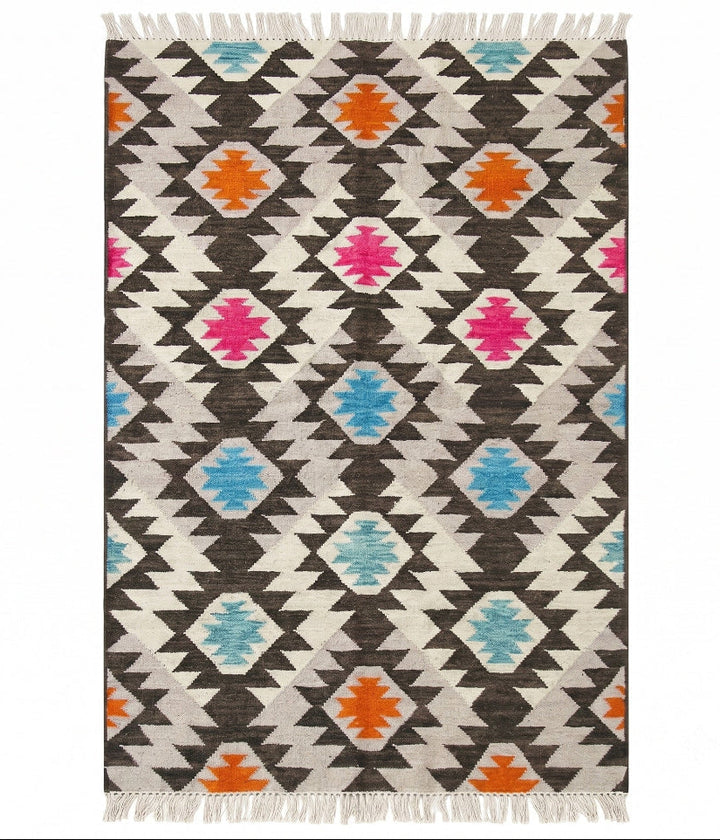 A rectangular woven area rug with a Southwestern geometric pattern, featuring dark brown, cream, black, orange, pink, and light blue diamond motifs with white fringe on the top and bottom.