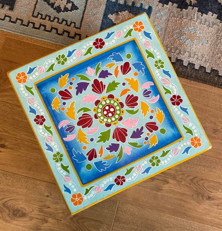 Decorative square table with colourful floral patterns on a wooden floor.