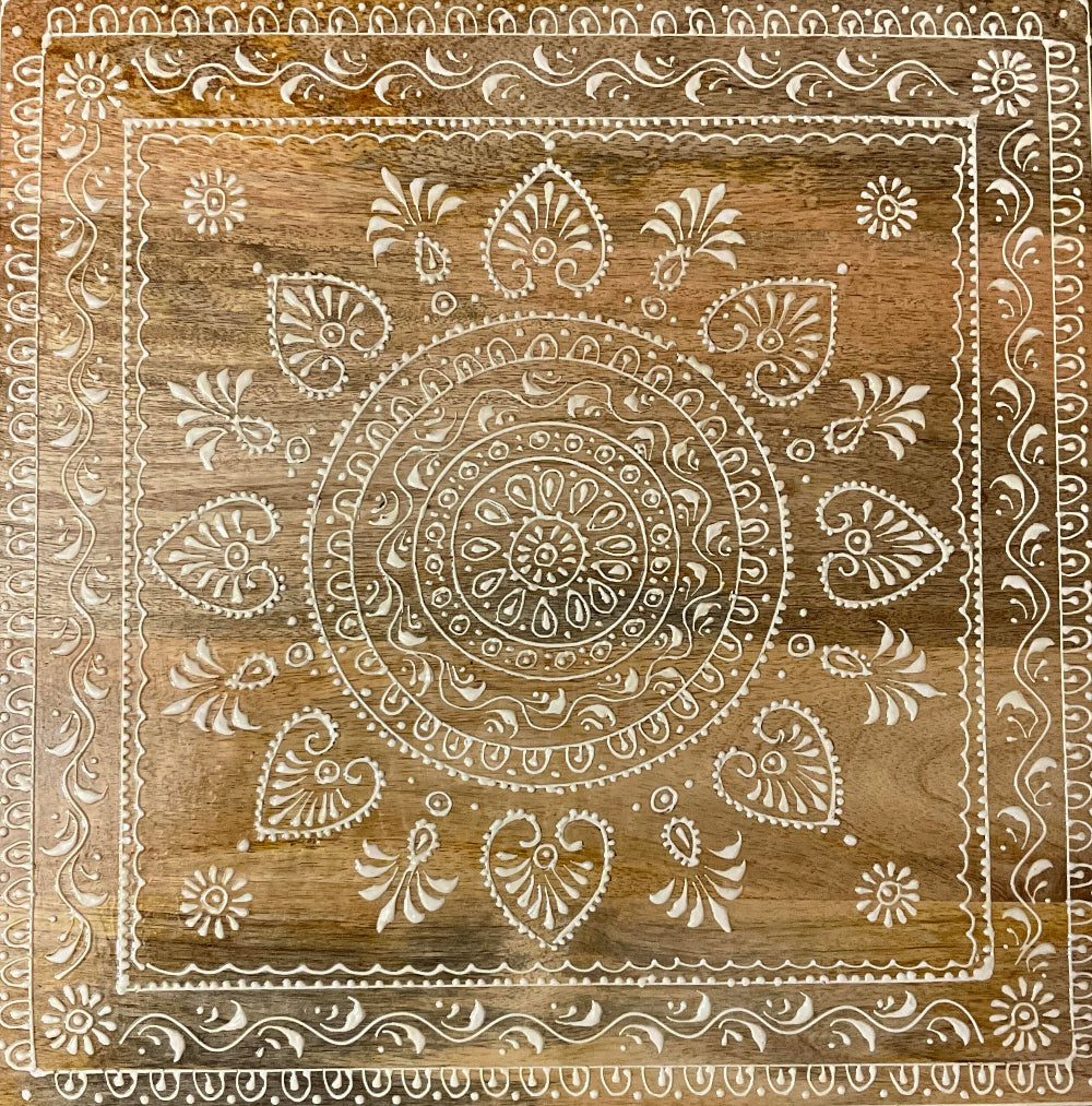Decorative wooden panel with intricate white hand painted design on a brown wooden table background