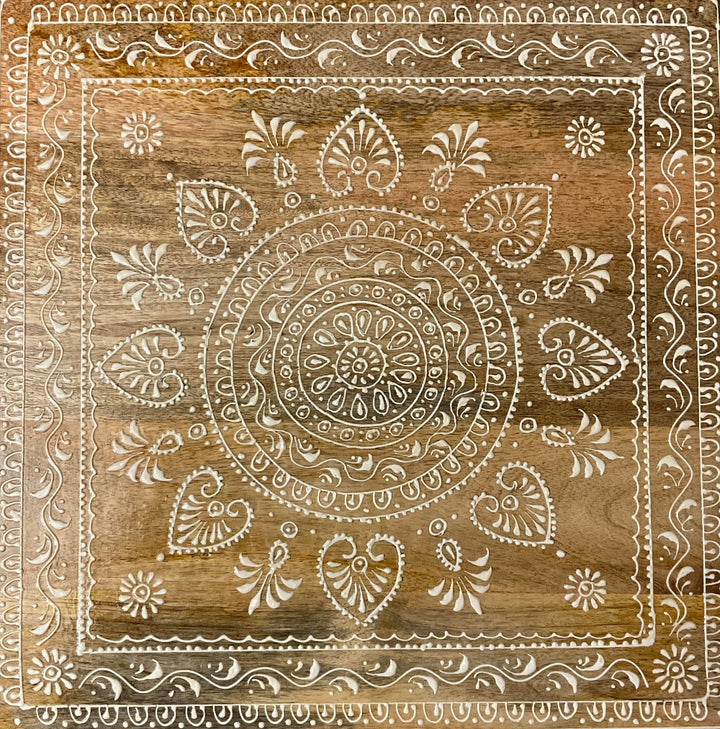 Decorative wooden panel with intricate white hand painted design on a brown wooden table background
