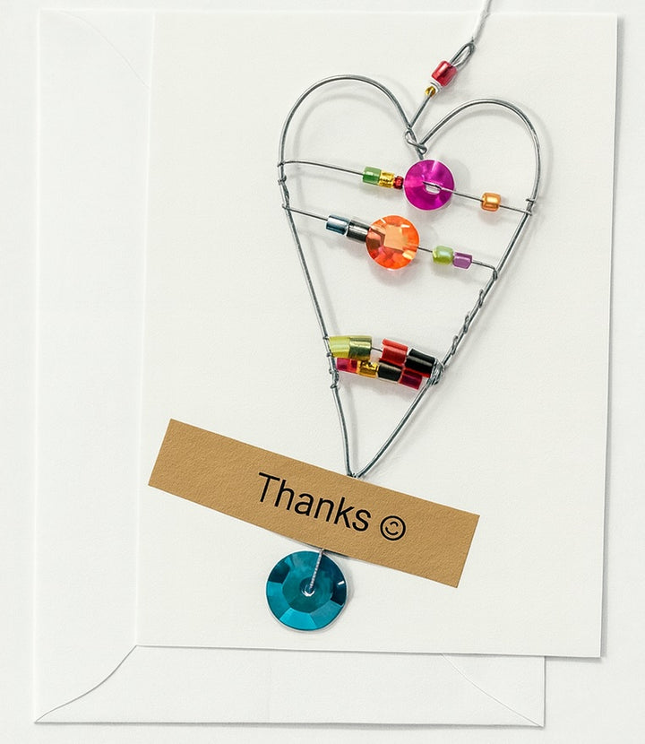 Heart-shaped decorative item with colorful beads and a 'Thanks' card on a white background