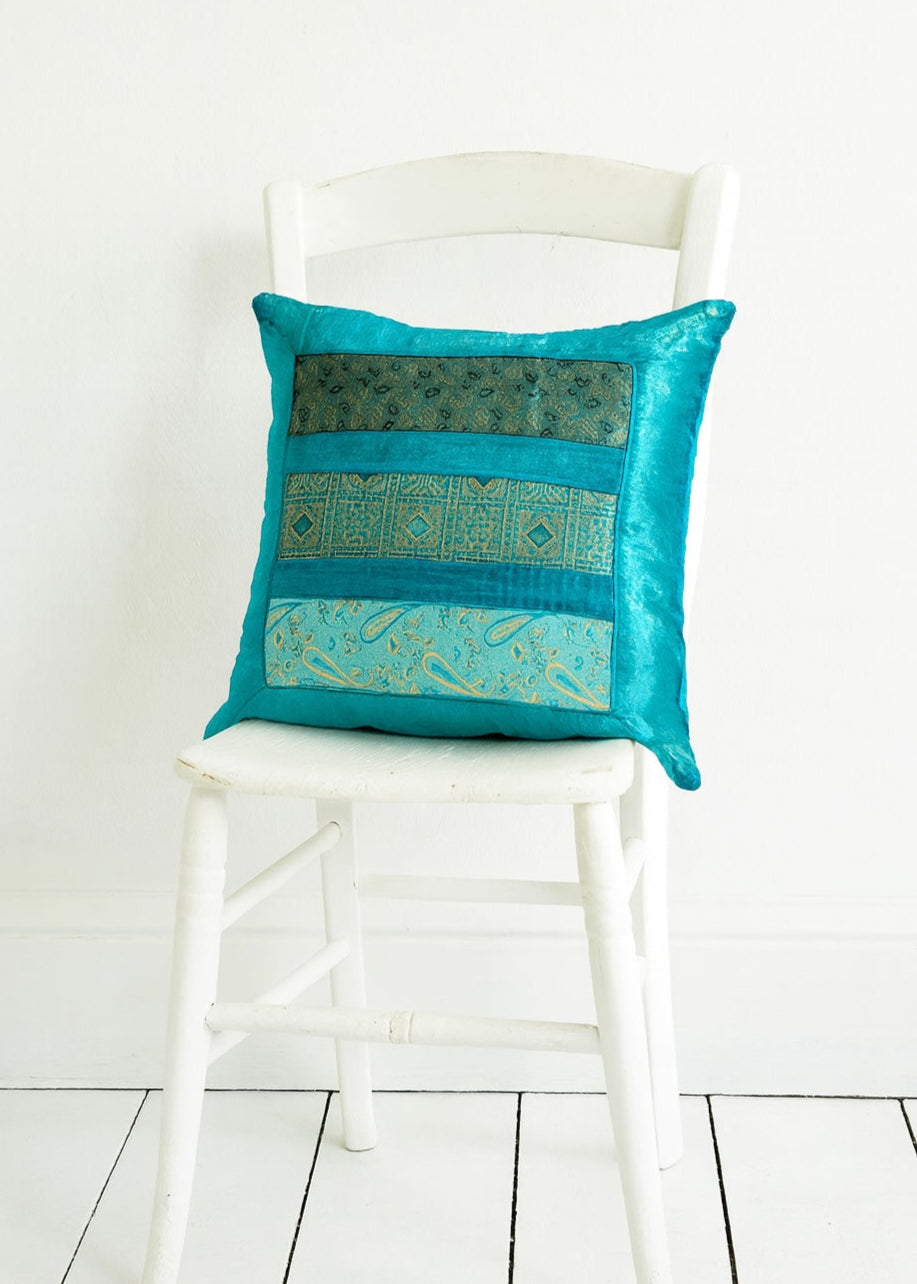 Turquoise decorative pillow with gold patterns on a white chair against a white background