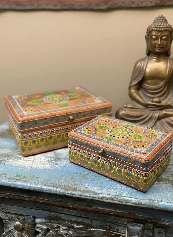 Decorative boxes with intricate designs on a table next to a Buddha statue.