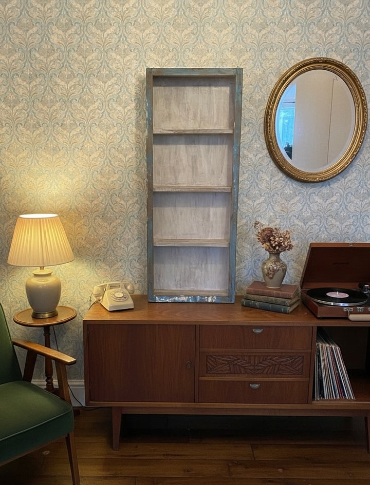 Nostalgic living room with wooden sideboard, lamp, and record player against patterned wallpaper with display cabinet.