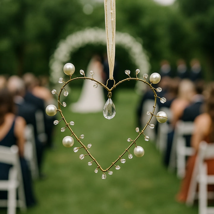 Decorative heart-shaped ornament with pearls and a teardrop hanging over a wedding aisle.