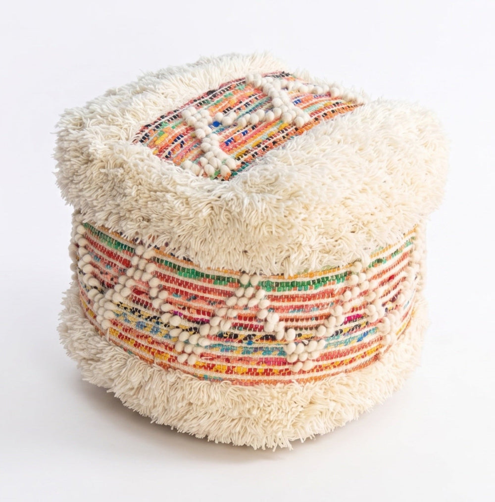 A small woven pouf or ottoman with a cream-colored shaggy top and sides, decorated with colorful geometric stripes in red, orange, yellow, green, and blue, shown on a plain white background.