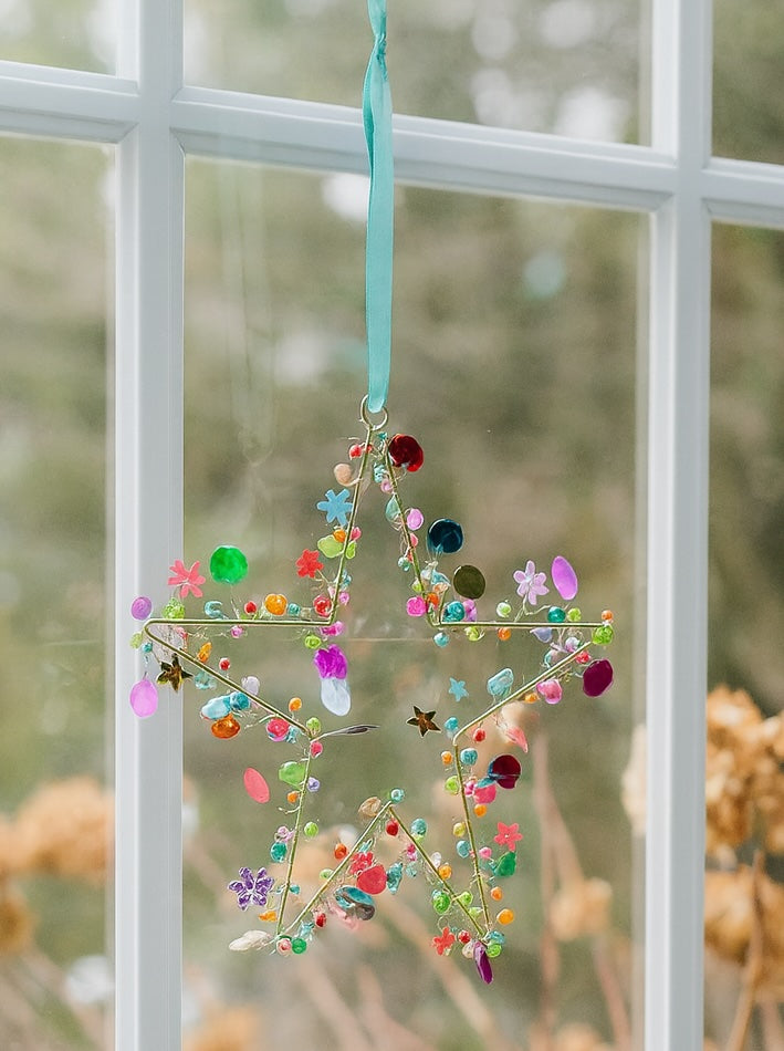 Decorative star-shaped ornament with colorful beads hanging on a window.
